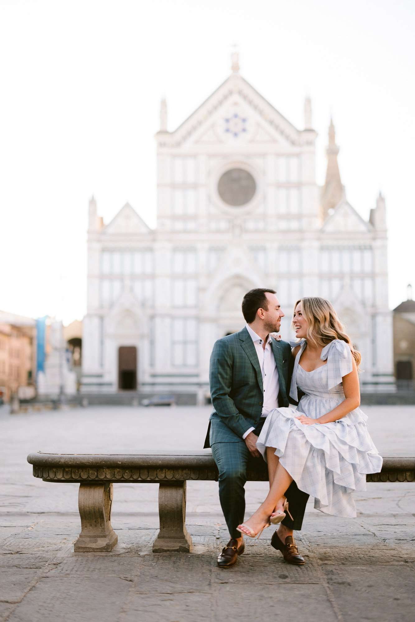 Engaged couple sitting on a stone bench in Piazza Santa Croce during an elegant engagement photoshoot in Florence.