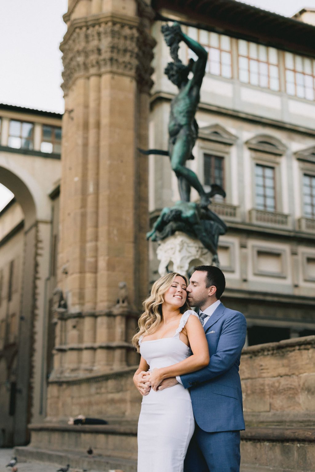 Romantic engagement photo of a couple embracing in Florence, with a historic fountain and Renaissance architecture in the background.
