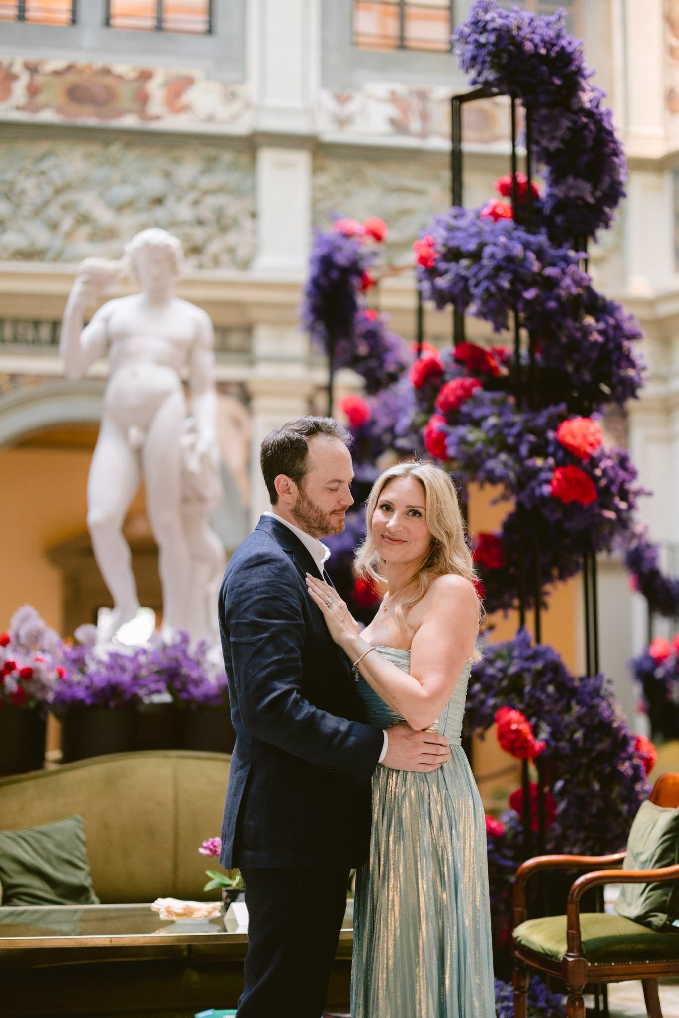 Anniversary portrait in the atrium Couple embracing beside purple and red flowers beneath the hotel skylight